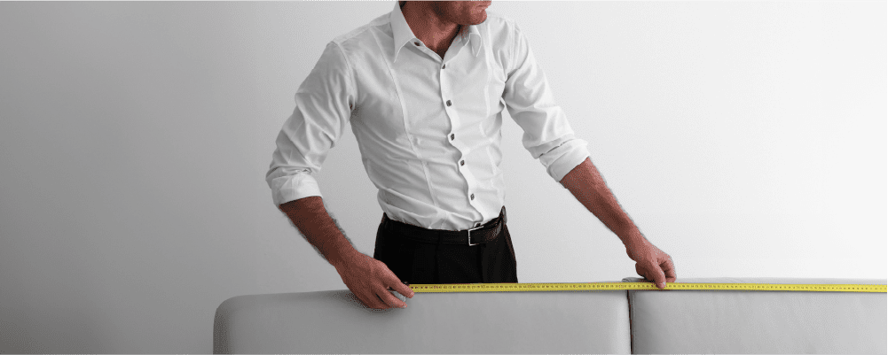 Een persoon die een meetlint gebruikt om de afmetingen van een groot meubelstuk, zoals een kast of bank, te meten.