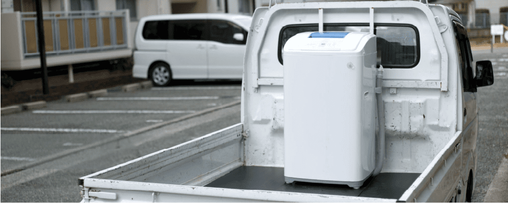 Afbeelding van een wasmachine, veilig vastgezet op een aanhangwagen met op de achtergrond een 1BOX storage faciliteit